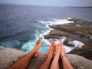 Low section of couple relaxing on rock at beach