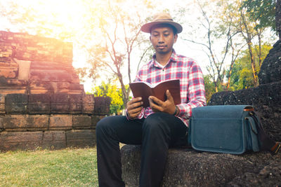 Young man reading book while sitting on land