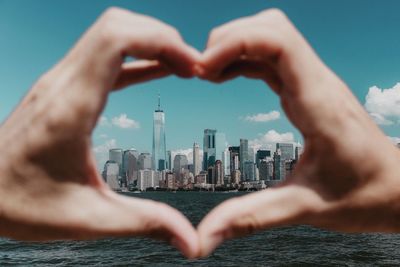 Close-up of hand making heart shape against building in city