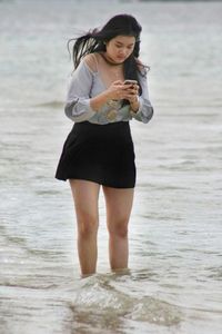 Full length of young woman using mobile phone at beach