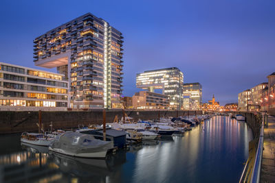 Sailboats moored on harbor by buildings against sky at night