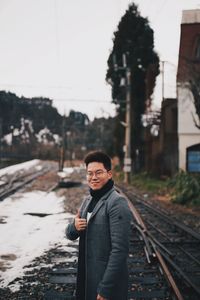 Portrait of young man standing on railroad track during winter