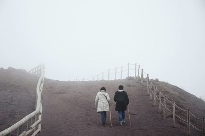 Rear view of hikers walking on field against sky during foggy weather