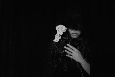 Close-up of young woman holding flower over black background