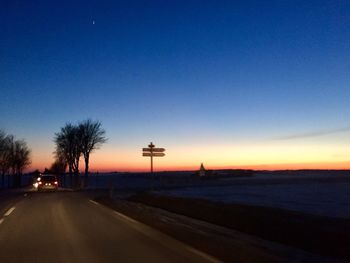 Road by trees against sky during sunset