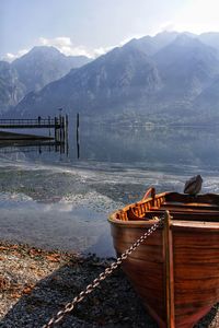 Boat moored at lakeshore with mountains in background against sky