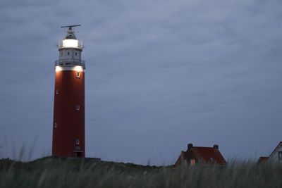 Lighthouse on field by building against sky at dusk