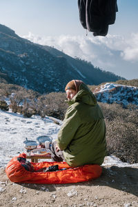 Man sitting on snowy mountain against sky