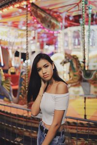 Portrait of young woman standing illuminated amusement park ride at night