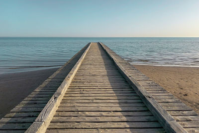 Boardwalk leading towards sea against clear sky