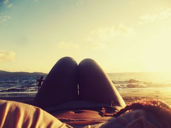 Low section of woman relaxing on beach against sky