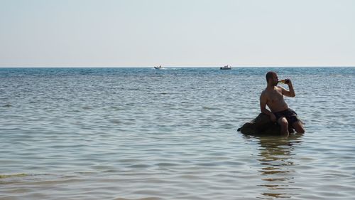 People sitting in sea against clear sky