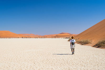 Full length of woman walking on desert against clear sky