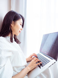 Side view of young woman using laptop while sitting at home