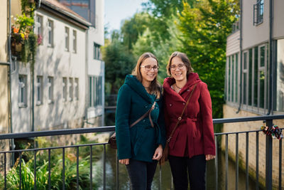 Portrait of smiling women standing on bridge against buildings in city