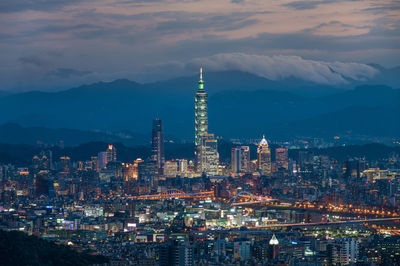 Illuminated buildings in city against cloudy sky