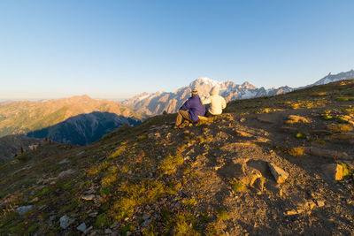 Rear view of people sitting on mountain against clear sky