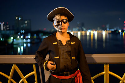 Portrait of young man wearing pirate costume standing on bridge at night