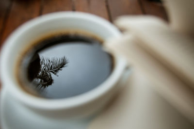 Close-up of coffee cup on table with reflection of a palm tree next to the book