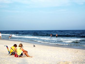 People enjoying at sandy beach against sky