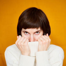 Portrait of young woman covering face against yellow background