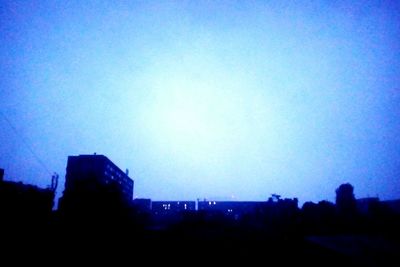 Silhouette city against clear blue sky at night