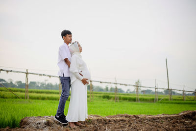 Full length of young man and pregnant woman standing on field