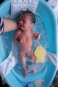 Cropped image of mother bathing newborn baby boy in bathtub