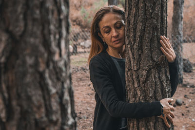 Full length of woman standing by tree trunk in forest