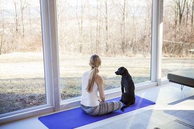 Rear view of woman sitting with dog on exercise mat at home