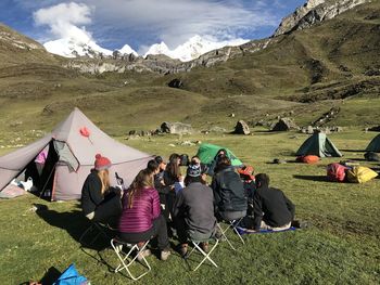 People sitting on field by mountains against sky