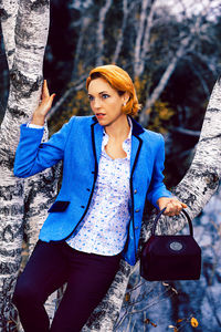 Woman looking away while standing by tree trunk