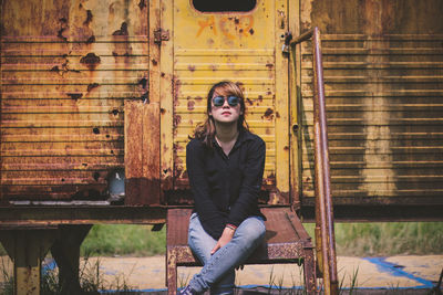 Portrait of young woman sitting against abandoned metal house