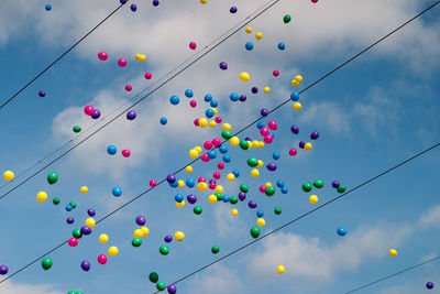Low angle view of colorful helium balloons flying over cables against sky