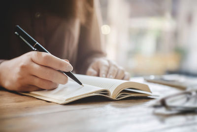 Midsection of woman reading book on table