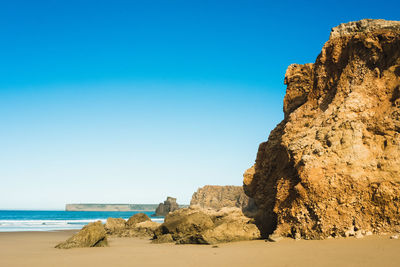 Rock formations on beach against clear blue sky