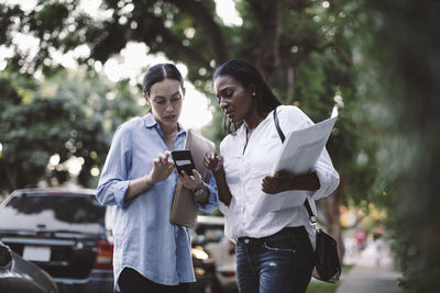 Low angle view of entrepreneur showing smart phone to coworker while standing outdoors