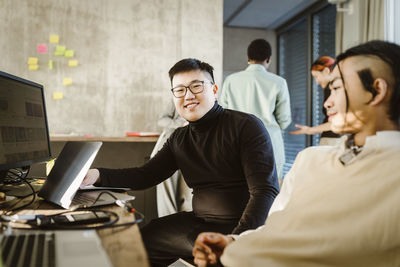 Portrait of smiling programmer sitting with colleague at desk in creative office