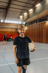 Smiling boy with disability holding soccer ball while standing at sports court