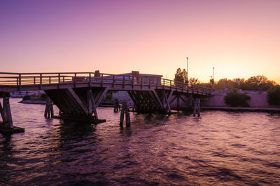 Pier over river against sky during sunset