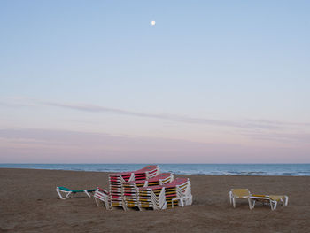 Chairs on beach against sky during sunset