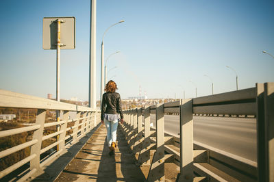 Rear view of young woman walking on bridge against sky