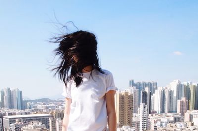 Woman with tousled hair standing on building terrace against city