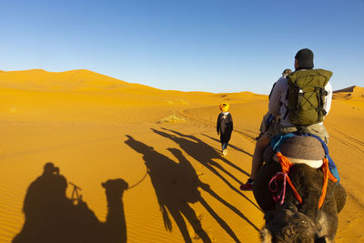 Rear view of people riding camel at desert