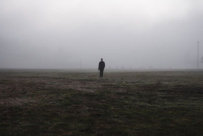 Full length of man standing on landscape against sky during foggy weather