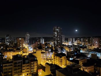 Illuminated modern buildings in city against sky at night