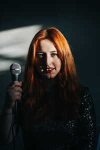 Portrait of redhead female singer woman in sparkly evening dress holding microphone on dark night