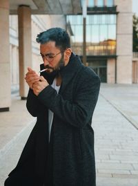 Young man igniting cigarette while standing outdoors