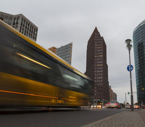 Cars on road by buildings against sky in city
