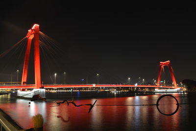 Illuminated suspension bridge over river against sky at night